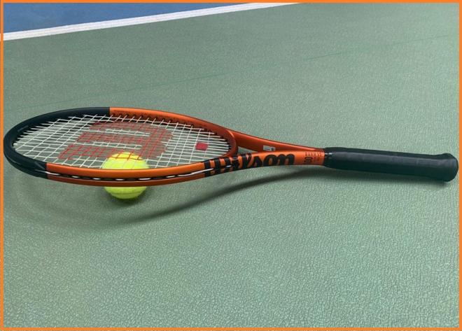 La raquette WILSON BURN 100 V5.0 avec son habillage orange métallisé et noir, lors de notre test - © Tennisleader.fr